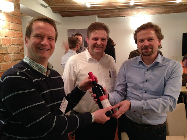 Hannover, Germany on February 11th 2016: After losing the MbT bet, Tim Weilkiens (on the right) hands over a bottle of wine on to Jesko Lamm (on the left) under the strict supervision of “Gesellschaft für Systems Engineering”, represented by its president (in the middle). Photo: ©2016 Gesellschaft für Systems Engineering, reproduced with permission.